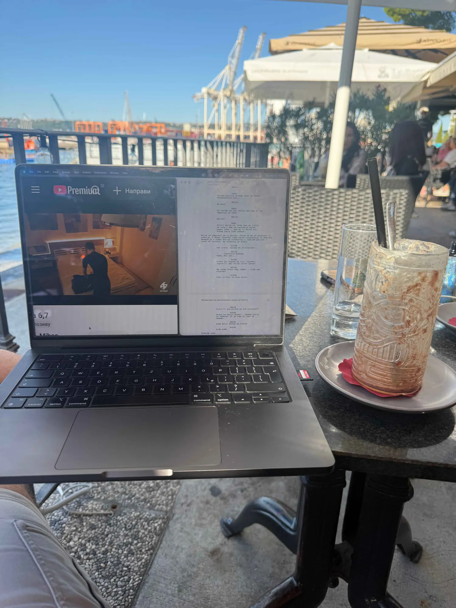 Laptop sa otvorenim filmskim scenarijom na stolu kafića pored luke